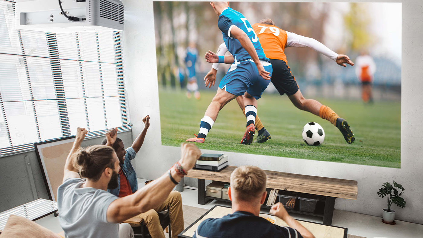 Three men cheering while watching soccer on a projector screen.