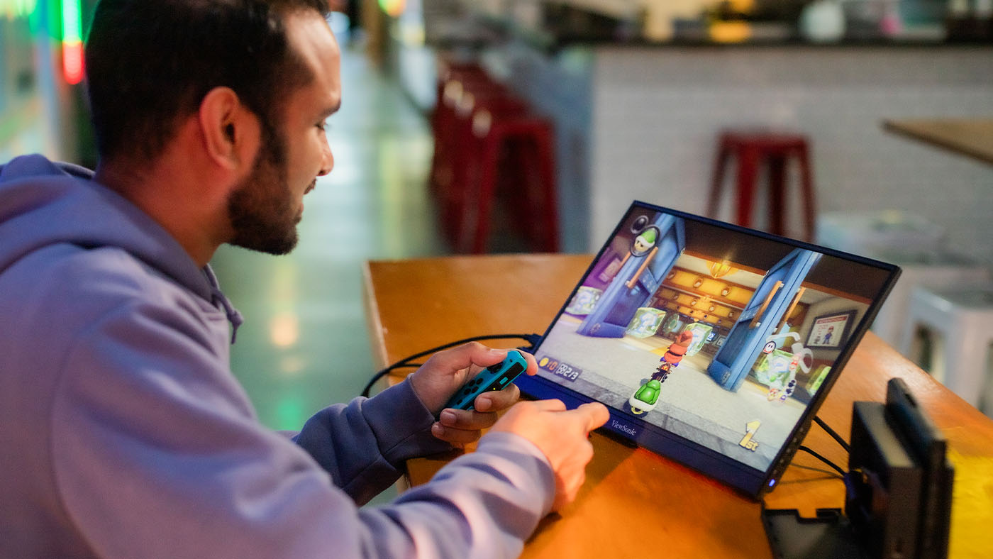 A man playing Mario Cart on a portable ViewSonic VX1754 monitor.