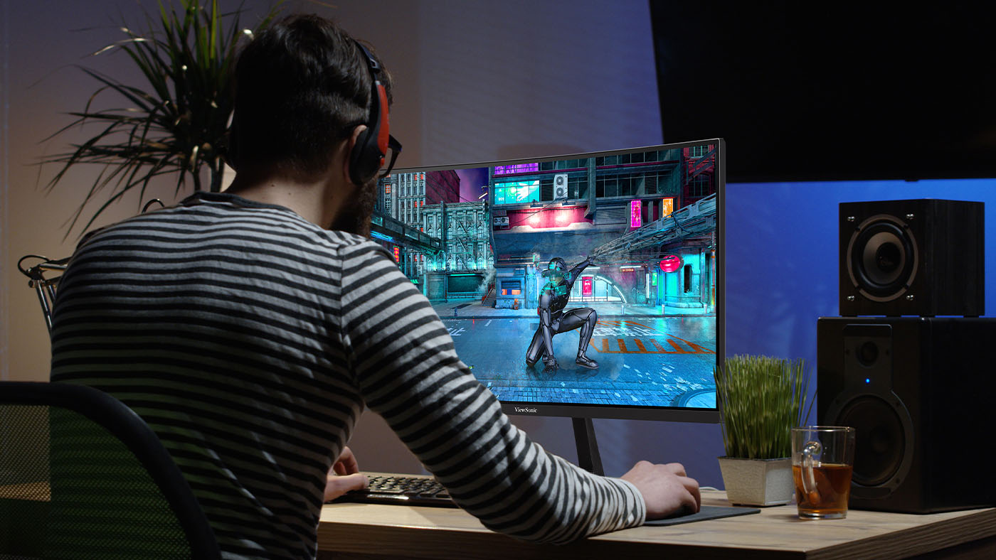 A man in a striped shirt sitting in front of a ViewSonic gaming monitor.