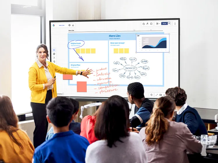 a teacher in front of a viewboard calling on a student with their hand raised