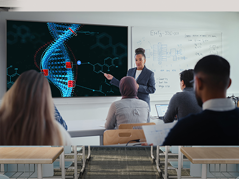 a teacher pointing to a DNA strand on a large screen at the front of a classroom