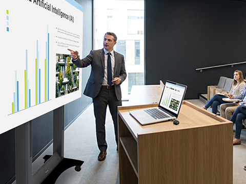 Male IT employee using laptop to manage various displays through the campus
