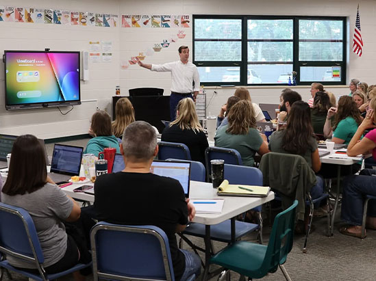a teacher stands in front of a classroom motioning at a viewboard display
