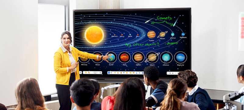 a teacher at the front of a classroom using the touch screen on a viewboard display to teach a lesson to a class full of students