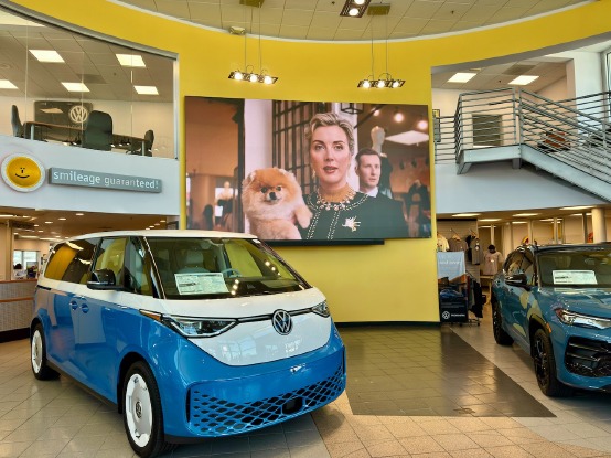 Owner of a VW dealership standing in the showroom next to a VW bus