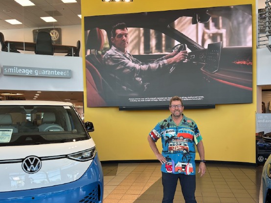 Owner of a VW dealership standing in the showroom next to a VW bus