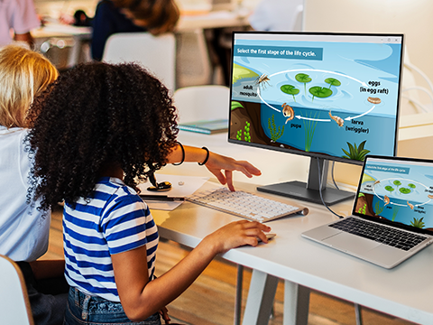 a child working at a laptop connected to a monitor in a classroom